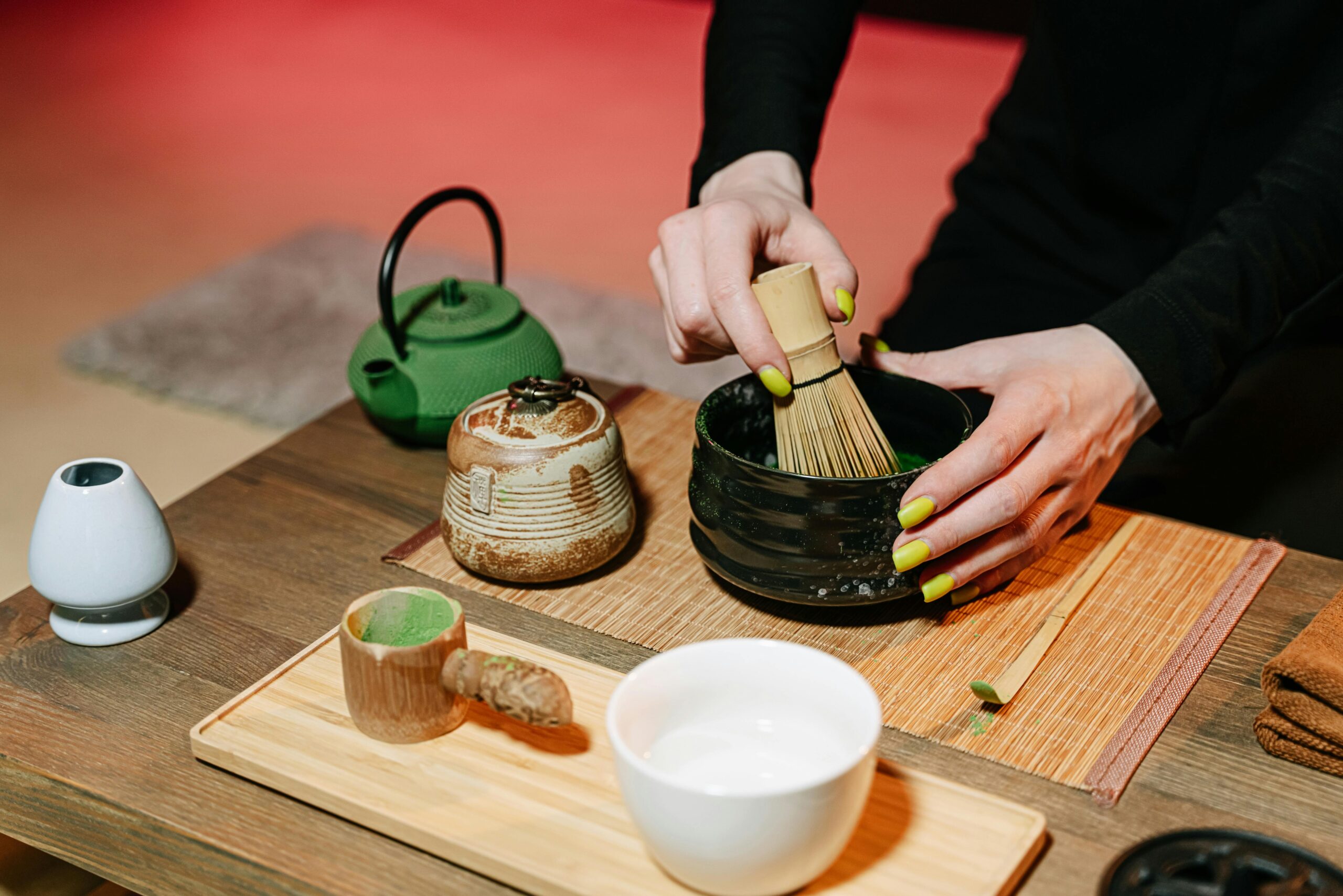 About Us Close-up of hands preparing matcha in a traditional Japanese tea ceremony with utensils.